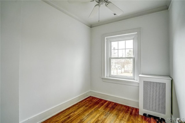 spare room featuring a ceiling fan, wood finished floors, baseboards, radiator heating unit, and crown molding