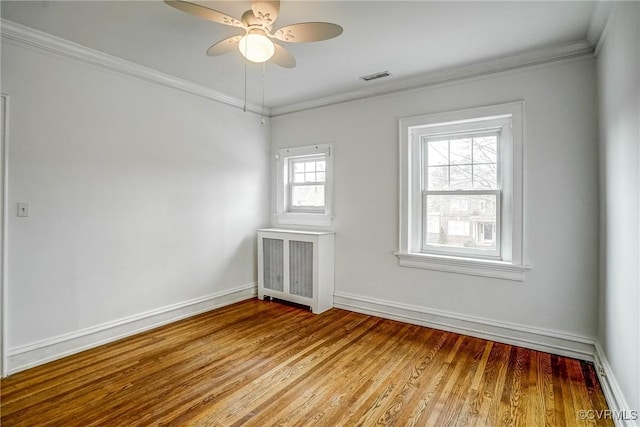 spare room featuring baseboards, wood finished floors, visible vents, and ornamental molding