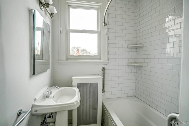 bathroom featuring a wealth of natural light, washtub / shower combination, and a sink