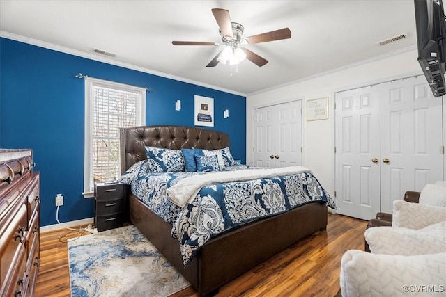 bedroom featuring wood finished floors, two closets, visible vents, and crown molding