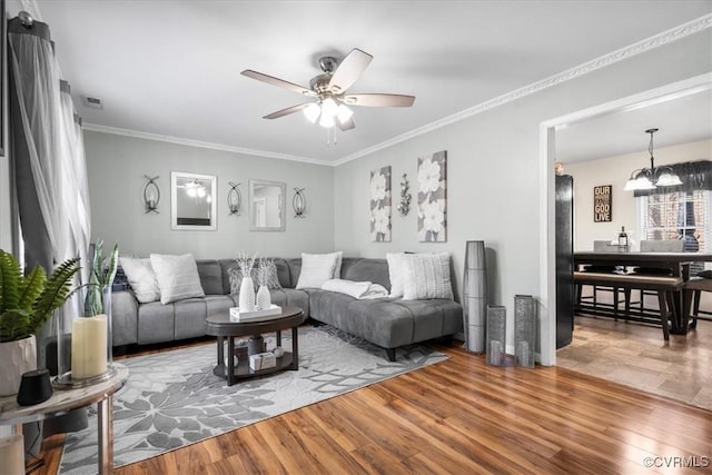 living room featuring ceiling fan with notable chandelier, crown molding, and wood finished floors