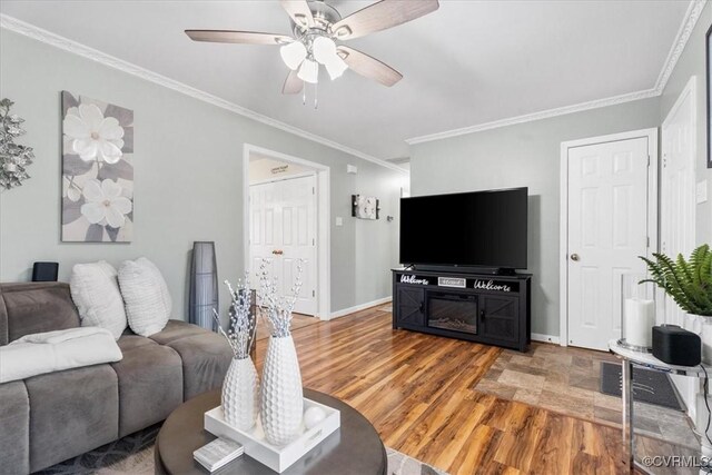 living room featuring ceiling fan, crown molding, baseboards, and wood finished floors