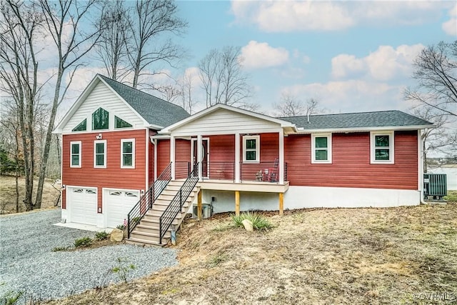 view of front facade with gravel driveway, a porch, a garage, cooling unit, and stairs