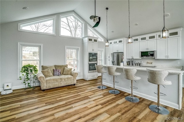 kitchen featuring a breakfast bar area, light wood finished floors, stainless steel appliances, light countertops, and white cabinetry