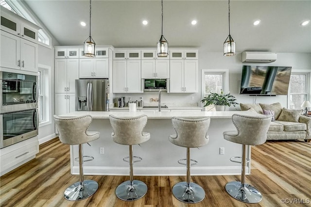 kitchen with appliances with stainless steel finishes, open floor plan, wood finished floors, light countertops, and a wall mounted AC