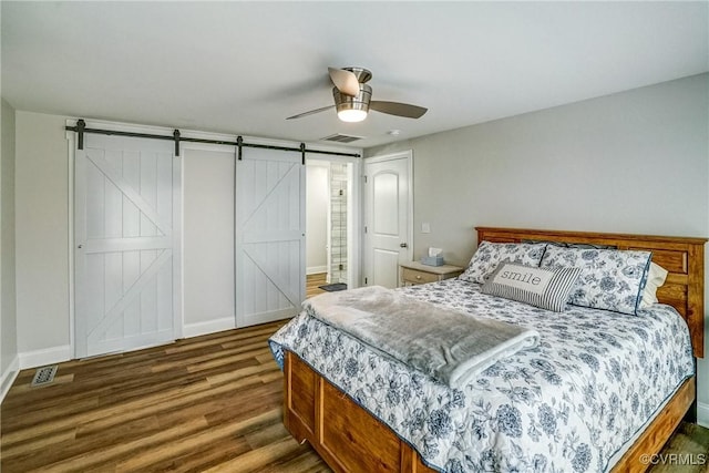 bedroom with visible vents, a barn door, a ceiling fan, wood finished floors, and baseboards