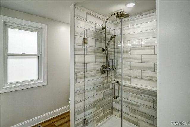 full bath featuring a stall shower, plenty of natural light, baseboards, and wood finished floors