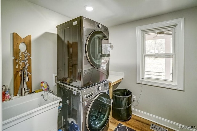 laundry room with laundry area, baseboards, visible vents, stacked washer and clothes dryer, and wood finished floors