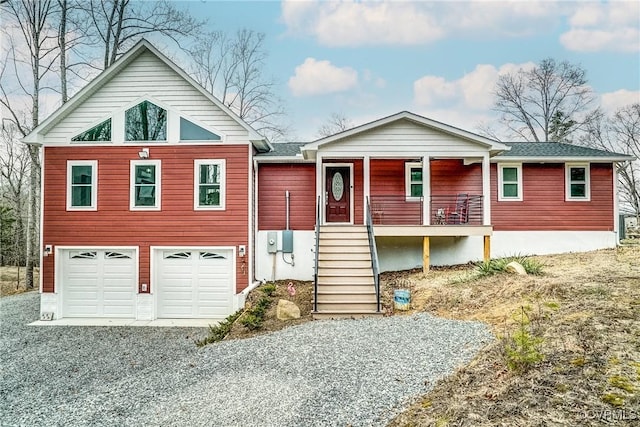 view of front of home featuring gravel driveway, covered porch, an attached garage, and stairs