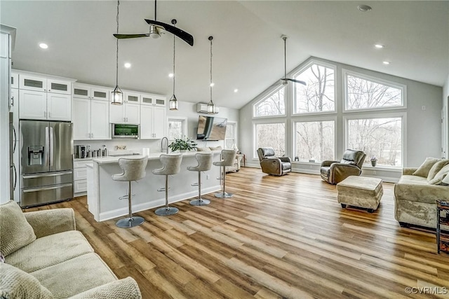 living area featuring light wood finished floors, baseboards, high vaulted ceiling, and recessed lighting