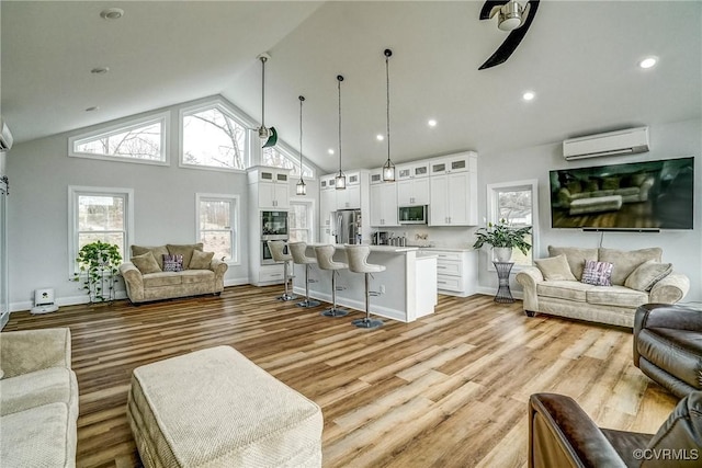 living area with high vaulted ceiling, a wall mounted AC, light wood-style flooring, and baseboards