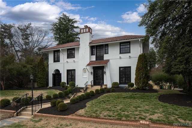 mediterranean / spanish house with a front lawn, a tiled roof, stucco siding, french doors, and a chimney