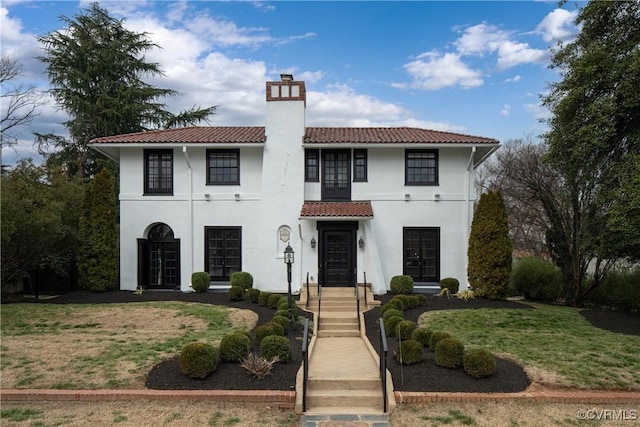 mediterranean / spanish-style house with a tile roof, stucco siding, french doors, and a chimney