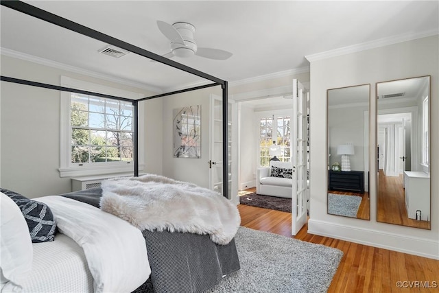 bedroom with crown molding, wood finished floors, visible vents, and baseboards