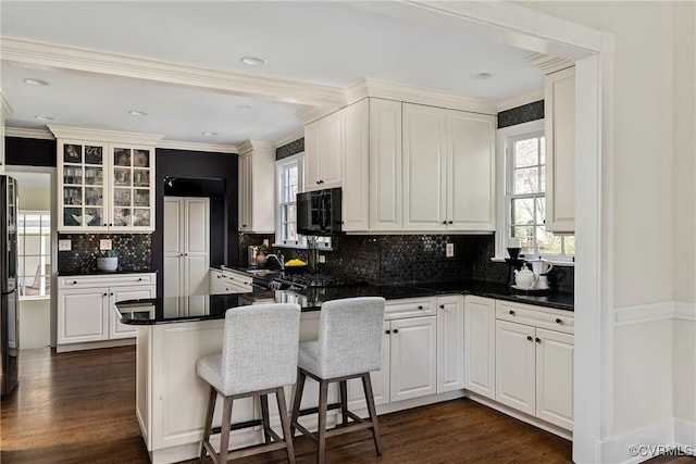 kitchen featuring dark countertops, a peninsula, glass insert cabinets, and dark wood-type flooring