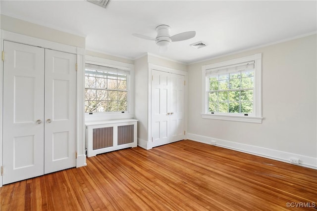 unfurnished bedroom with visible vents, light wood-type flooring, two closets, radiator, and baseboards