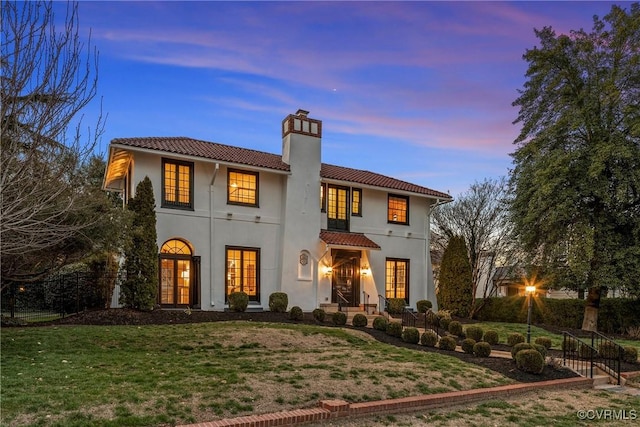 back of house at dusk featuring stucco siding, a chimney, french doors, a tile roof, and a lawn