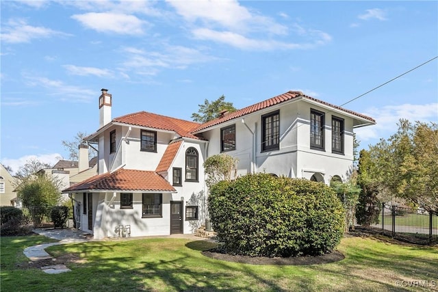 back of house featuring stucco siding, a lawn, a tile roof, fence, and a chimney