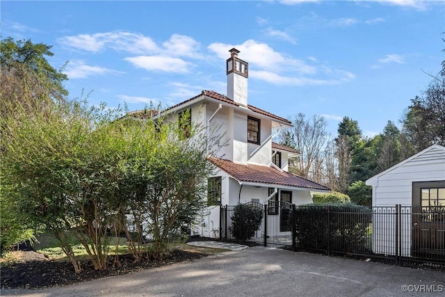 view of side of property with a fenced front yard, stucco siding, a chimney, and a tile roof