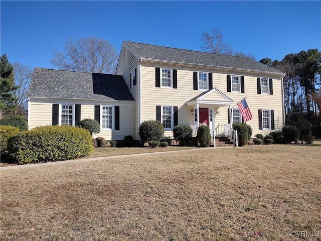 colonial inspired home with roof with shingles and a front yard