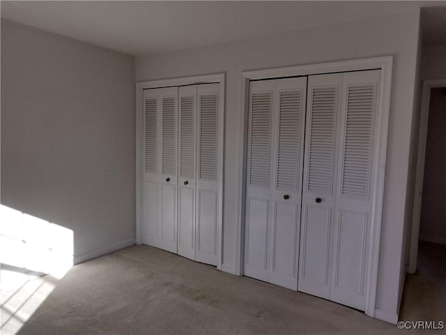 unfurnished bedroom with baseboards, light colored carpet, and multiple closets