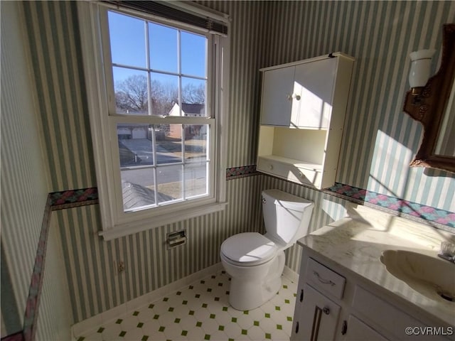 half bathroom with toilet, wallpapered walls, baseboards, and vanity