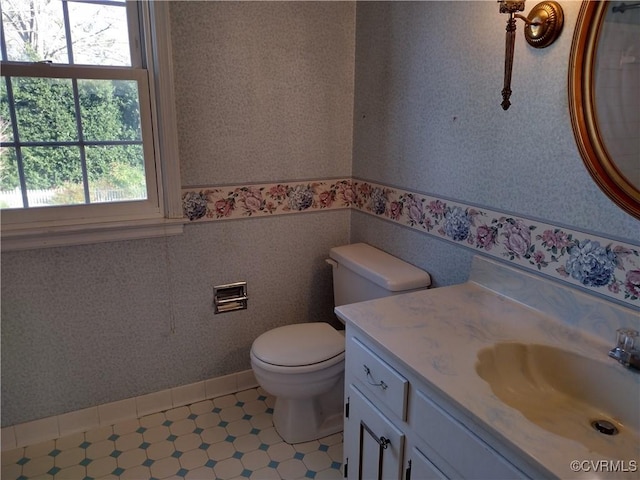 bathroom with toilet, wallpapered walls, a wainscoted wall, and vanity