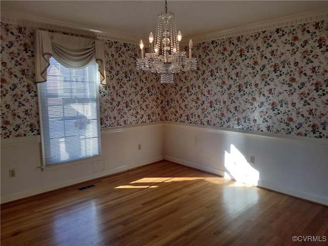 unfurnished room with a notable chandelier, wood finished floors, visible vents, wainscoting, and wallpapered walls