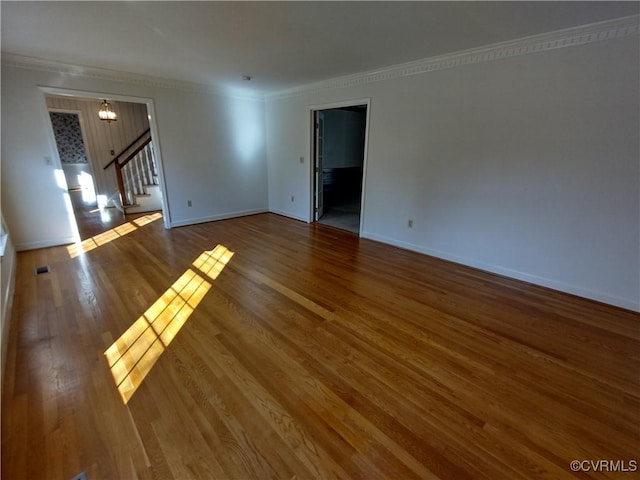 spare room featuring baseboards, stairway, wood finished floors, and crown molding