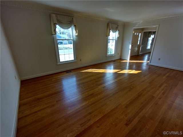 empty room featuring visible vents, crown molding, baseboards, and wood finished floors