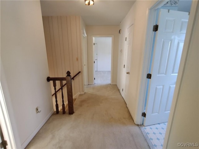 corridor featuring baseboards, an upstairs landing, and light colored carpet