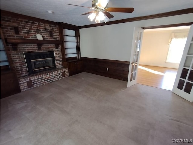 unfurnished living room featuring a wainscoted wall, ornamental molding, french doors, carpet floors, and a brick fireplace