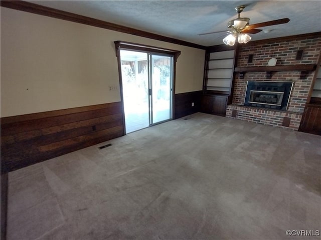 unfurnished living room with wooden walls, a wainscoted wall, ornamental molding, a brick fireplace, and carpet