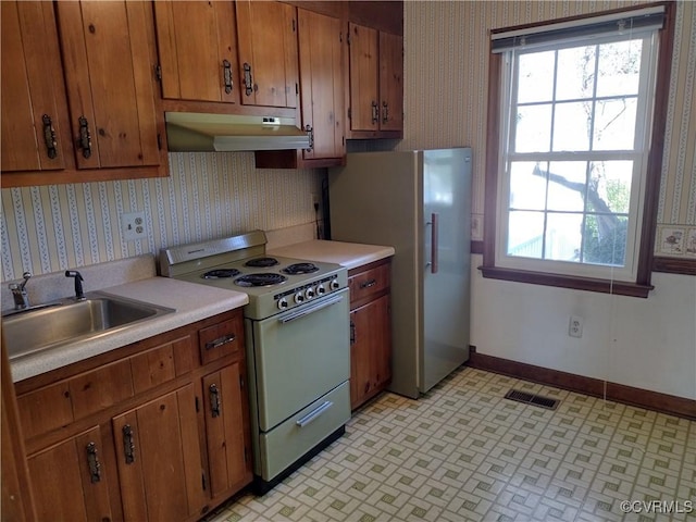 kitchen featuring white range with electric stovetop, light countertops, a sink, under cabinet range hood, and wallpapered walls