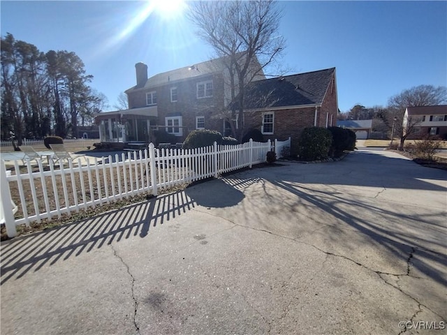 back of property with a fenced front yard, concrete driveway, brick siding, and a chimney