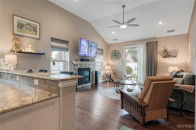 living area with visible vents, vaulted ceiling, dark wood-style floors, a glass covered fireplace, and a ceiling fan