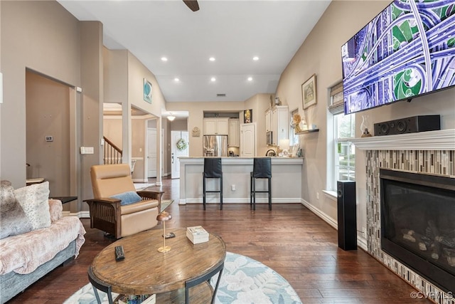 living area with baseboards, lofted ceiling, recessed lighting, a glass covered fireplace, and dark wood-style flooring