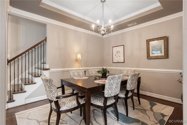 dining area featuring a tray ceiling, a notable chandelier, visible vents, and wood finished floors