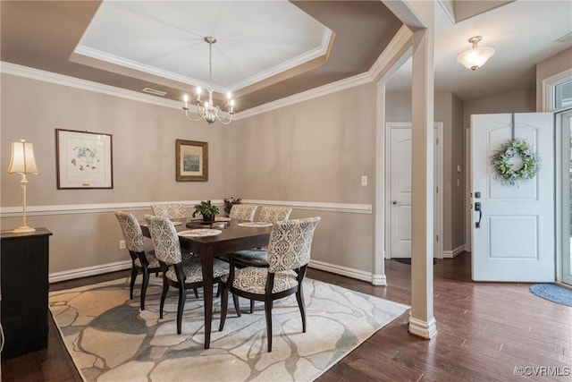 dining area featuring a notable chandelier, ornamental molding, a tray ceiling, wood finished floors, and baseboards