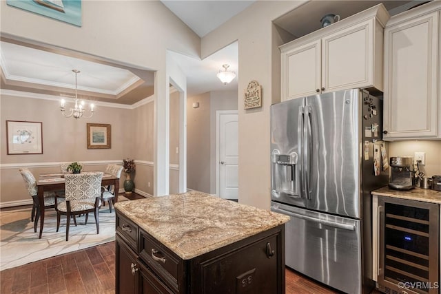 kitchen featuring light stone counters, dark wood finished floors, wine cooler, stainless steel refrigerator with ice dispenser, and a raised ceiling