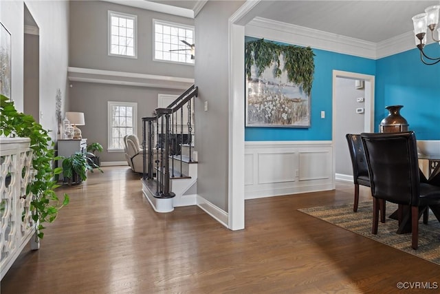 entrance foyer featuring wood finished floors, an inviting chandelier, stairs, crown molding, and a decorative wall