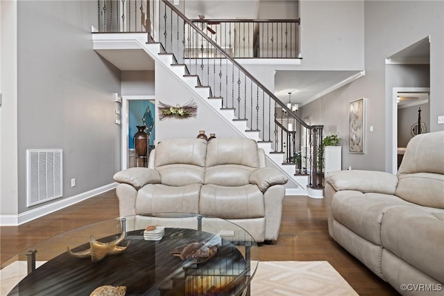 living area with visible vents, stairway, a high ceiling, wood finished floors, and baseboards