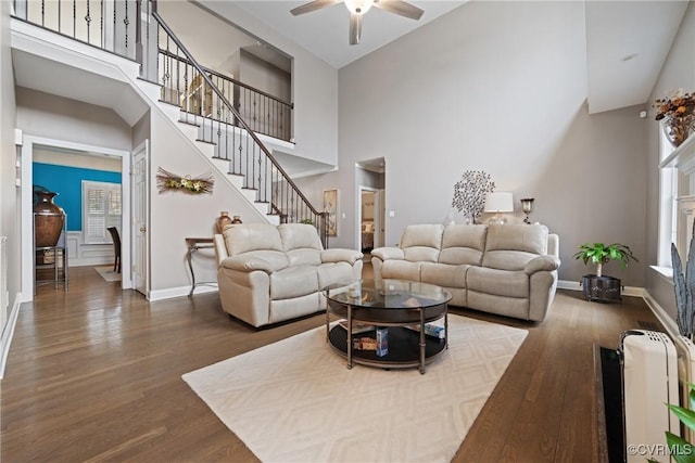 living room featuring stairs, a towering ceiling, baseboards, and wood finished floors