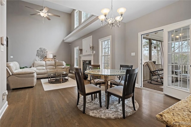 dining area with ceiling fan with notable chandelier, dark wood-style flooring, a high end fireplace, and baseboards