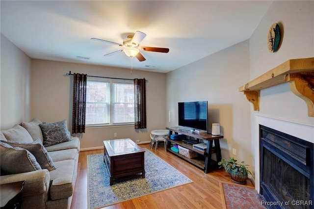 living room with ceiling fan, wood finished floors, a fireplace with flush hearth, visible vents, and baseboards