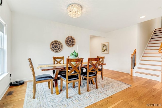 dining space featuring visible vents, light wood-style flooring, stairway, an inviting chandelier, and baseboards