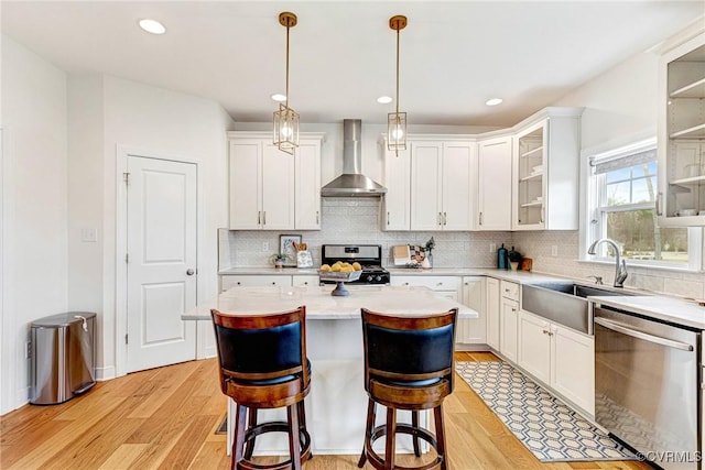 kitchen featuring a kitchen island, light wood-style flooring, a sink, stainless steel appliances, and wall chimney range hood