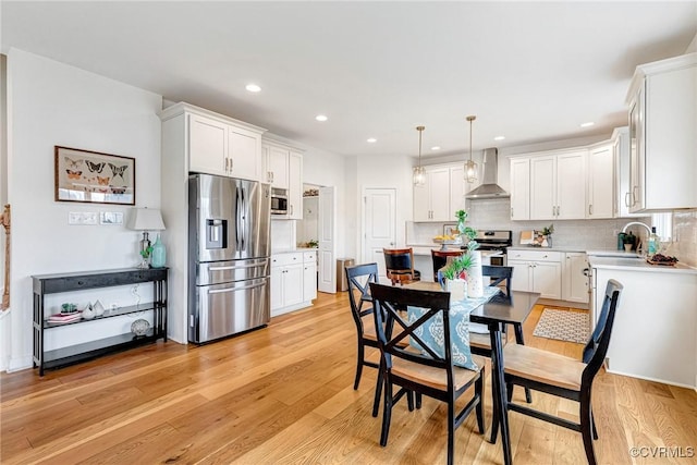 kitchen featuring light wood-style floors, appliances with stainless steel finishes, light countertops, and wall chimney range hood