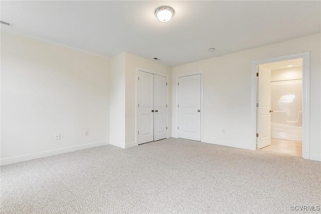 unfurnished bedroom with ensuite bathroom, light colored carpet, baseboards, and a closet