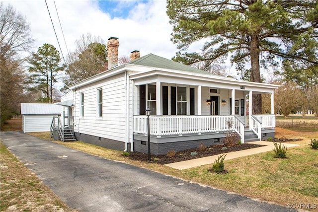 view of front of home with crawl space, covered porch, a chimney, and a detached garage